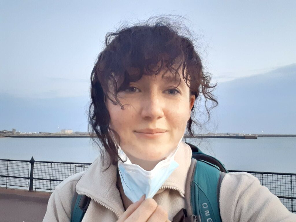 Sophie stands in front of the camera, on a pier, wearing a face mask.