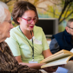 Volunteer assisting an senior lady by reading to her