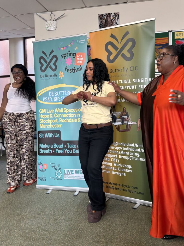 Three women on stage, presenting. They stand in front of banners promoting De Butterfly CIC