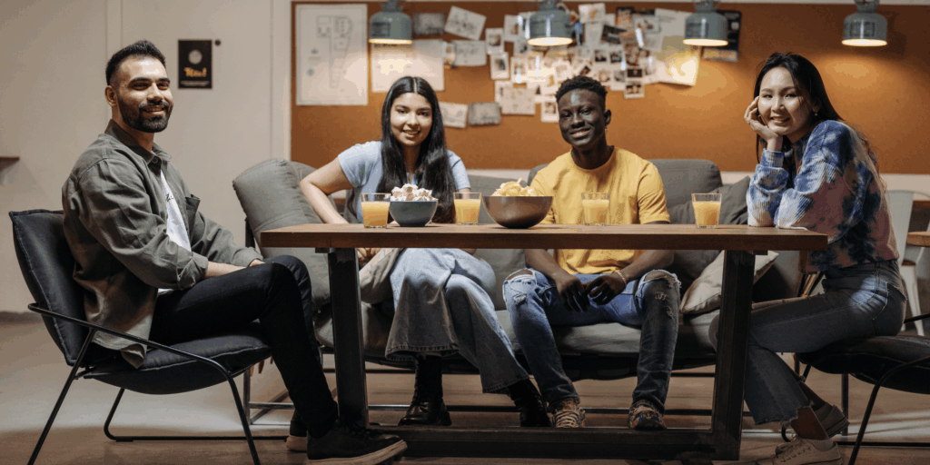 A group of diverse individuals sit around a table, smiling into the camera